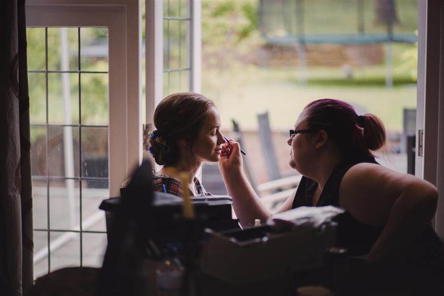Bride having her makeup done at a window with Ms Moo Make Up